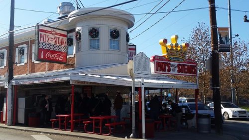 Exterior of Pat's King of Steaks, a popular eatery with outdoor seating and festive decorations, in a bustling urban setting.