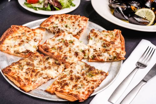 A plate of cheesy flatbread topped with sausage and green peppers, served with a side salad and mussels.
