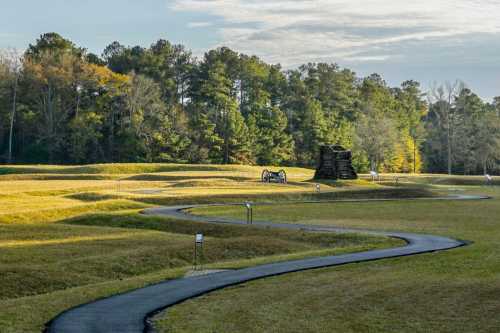 A winding path through a grassy landscape with trees and a stone structure in the background under a clear sky.