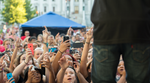 A crowd of excited fans holding up phones, capturing a performance on stage.