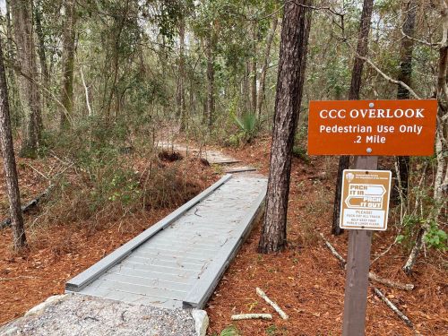 A wooden path leads into a wooded area, with signs indicating the CCC Overlook and pedestrian use only.
