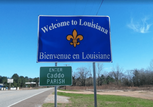 Welcome sign for Louisiana with a fleur-de-lis, featuring text in English and French, near Caddo Parish.