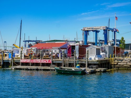 A waterfront scene featuring the Newport Lobster Shack and boats docked at a marina under a clear blue sky.