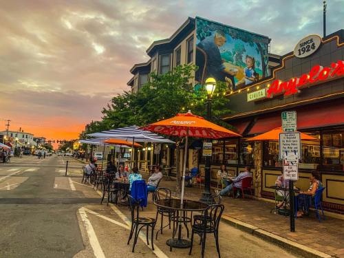 A street scene at dusk with outdoor dining, colorful umbrellas, and a mural on a building.