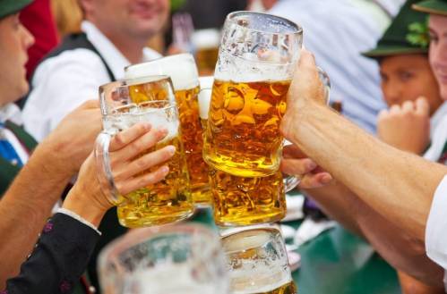 A group of people toasting with large beer mugs at a festive outdoor gathering.