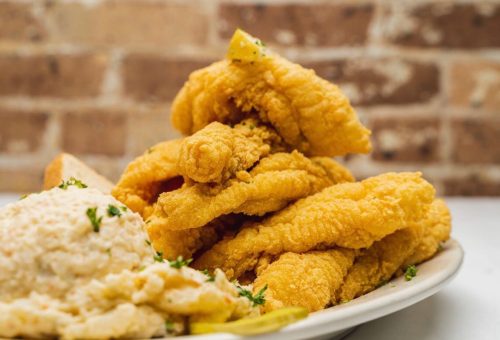 A plate of golden fried fish fillets stacked high, served with a side of creamy coleslaw and garnished with parsley.