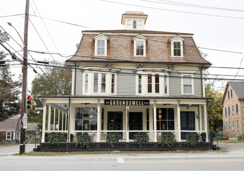 A large, historic building with a sloped roof and porch, featuring the sign "Groundswell" and surrounded by greenery.
