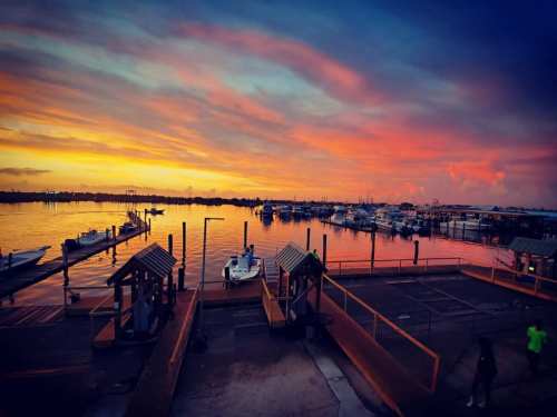 A vibrant sunset over a marina, with boats docked and colorful clouds reflecting on the water.