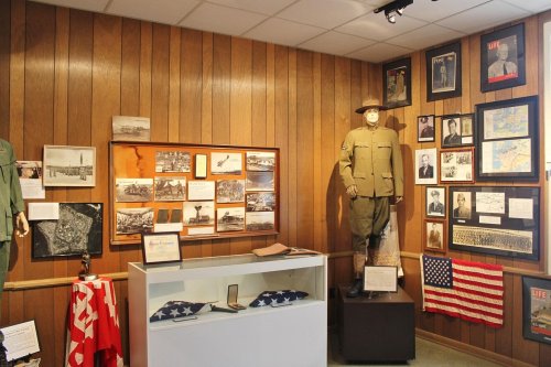 A museum display featuring military uniforms, photographs, and historical artifacts on wooden walls.