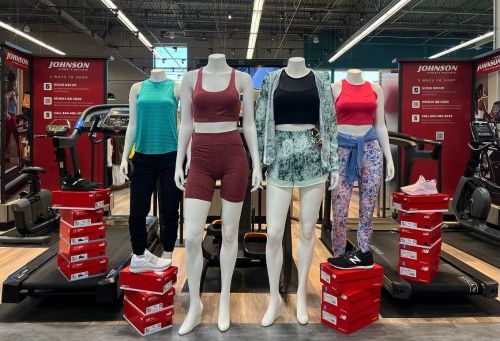 Four mannequins display athletic wear in a store, surrounded by shoe boxes and gym equipment.