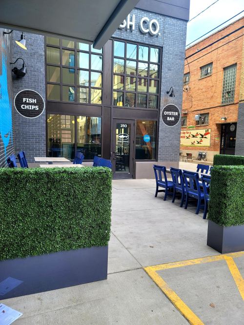 Exterior view of a restaurant named "Fish Co," featuring an oyster bar and outdoor seating with greenery.
