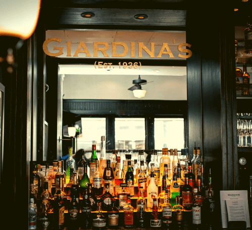 A bar display at Giardina's, featuring a variety of liquor bottles and a sign with the establishment's founding year.