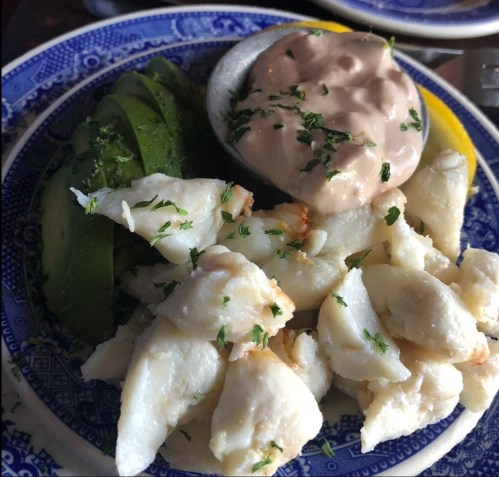 A plate with white fish, sliced avocado, and a creamy dipping sauce, garnished with herbs on a decorative blue plate.