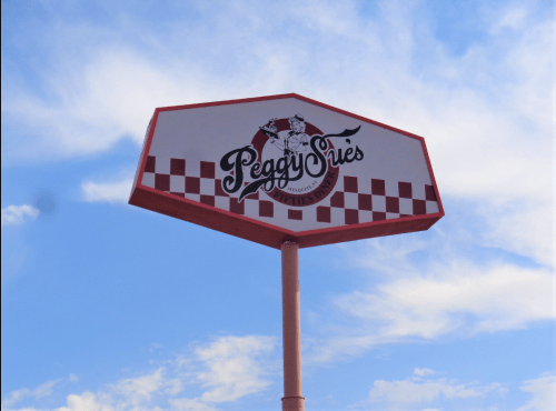 Sign for Peggy Sue's featuring a checkered pattern and a cowboy graphic against a blue sky.