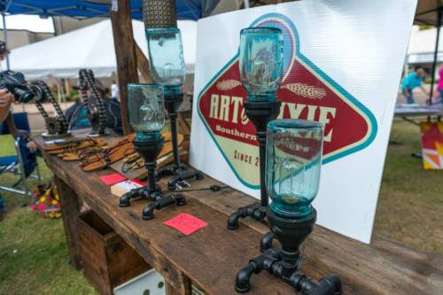 A wooden table displays unique lamps made from pipes and glass, with a sign reading "Art of Dixie" in the background.
