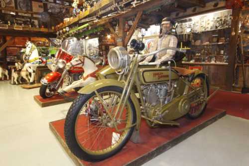 A vintage Harley-Davidson motorcycle displayed in a rustic setting, alongside another classic bike and various collectibles.