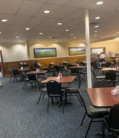 A spacious dining area with empty tables and chairs, featuring wooden accents and landscape paintings on the walls.