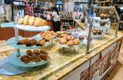 A display of various pastries and baked goods on a glass stand in a café setting.