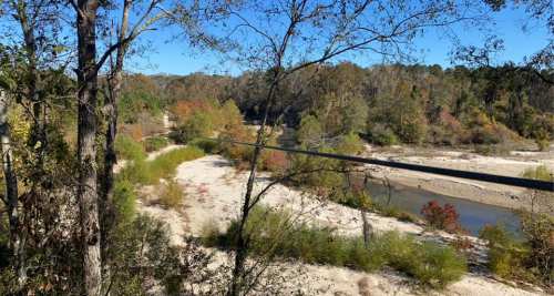 A serene landscape featuring a river winding through trees and sandy banks, with autumn foliage in the background.