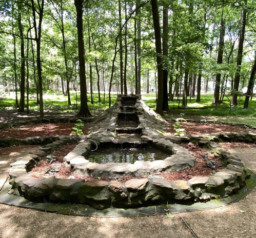 A serene stone fountain surrounded by trees and greenery in a peaceful park setting.