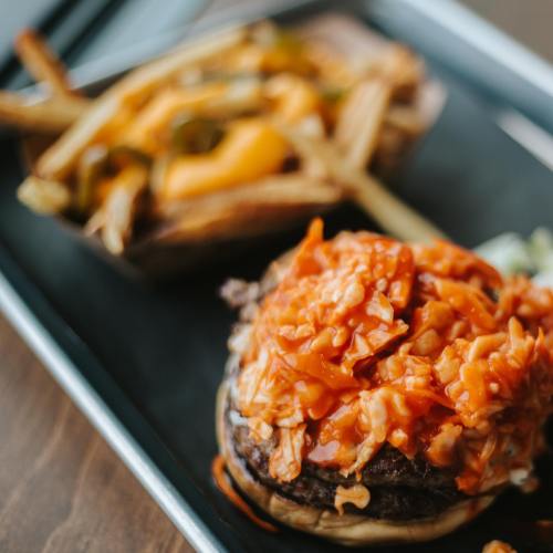 A close-up of a burger topped with shredded chicken and sauce, alongside a side of cheesy fries.