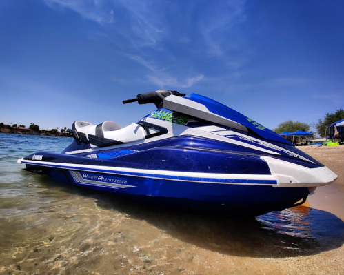 A blue and white jet ski parked on a sandy shore with clear water and a blue sky in the background.