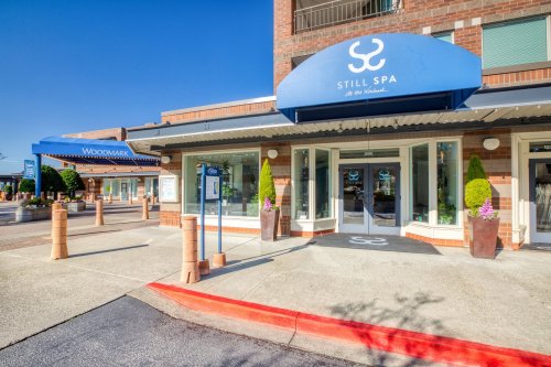 Exterior view of Still Spa with a blue awning, planters, and a clear sky in a shopping area.
