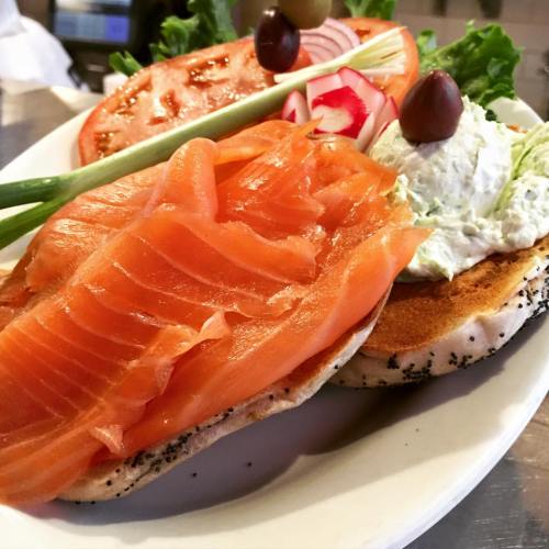 A plate featuring toasted bagel halves topped with smoked salmon, cream cheese, lettuce, tomato, and garnishes.