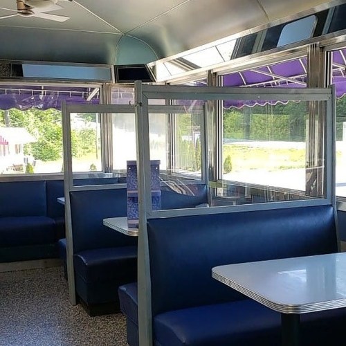 Interior of a diner with blue booths, white tables, and clear dividers, featuring large windows and purple awnings.