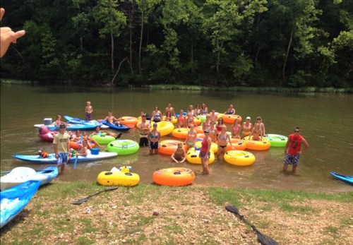 A group of people in colorful kayaks and tubes enjoying a sunny day on a river surrounded by trees.