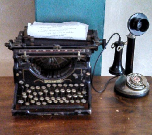 An antique Underwood typewriter next to a vintage telephone on a wooden table.