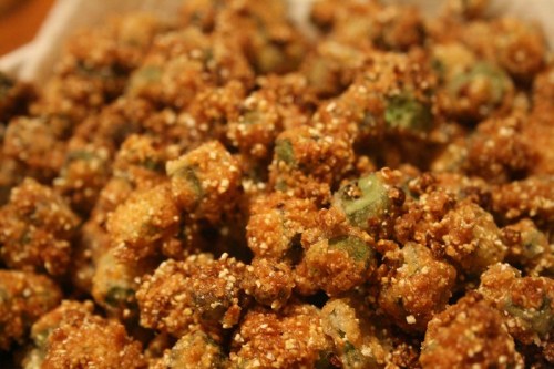 A close-up of crispy, golden-brown fried okra pieces, coated in a crunchy cornmeal crust.