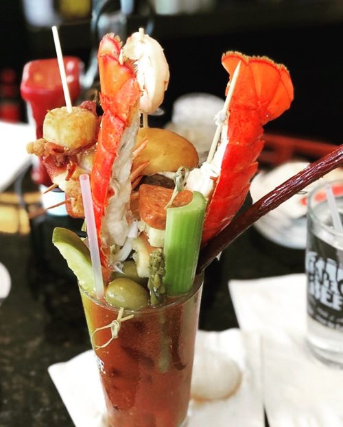 A tall glass filled with a colorful seafood cocktail, featuring shrimp, lobster, and various garnishes.