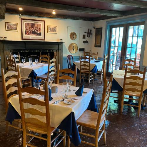 Cozy restaurant interior with wooden tables set for dining, featuring blue and white tablecloths and a fireplace.