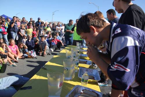 A competitive hot dog eating contest with participants focused on their plates, while a crowd watches eagerly.
