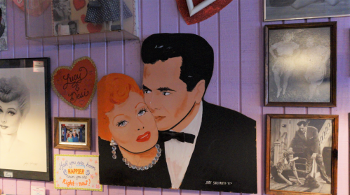 A colorful mural of a couple in vintage attire, surrounded by framed photos and decorations on a purple wall.
