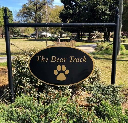 Sign for "The Bear Track" featuring a paw print, surrounded by greenery in a park-like setting.