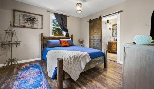 Cozy bedroom featuring a wooden bed, blue bedding, decorative rug, and a sliding barn door leading to a bathroom.