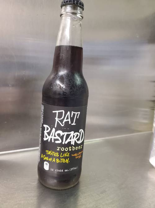 A bottle of "Rat Bastard" root beer with a humorous label, featuring bold text and a dark glass design.