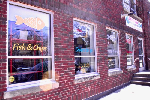 Exterior of a brick building featuring windows with signs for "Fish & Chips" and "Orders To Go."