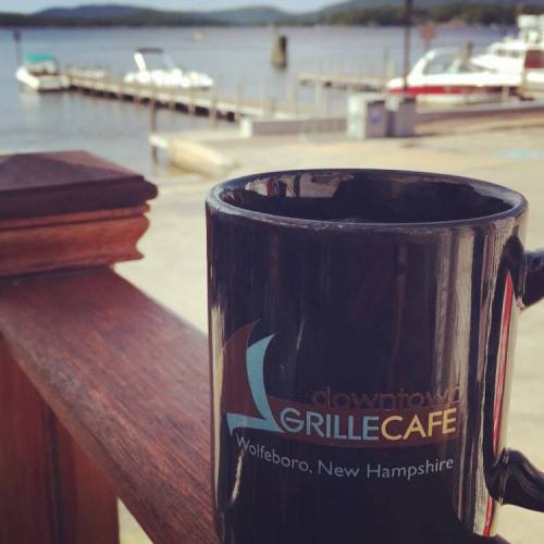 A coffee mug on a wooden railing with a scenic view of a lake and boats in the background.