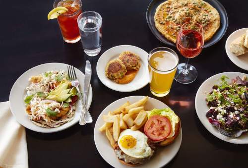 A table spread with various dishes: salads, burgers, drinks, and a pizza, showcasing a colorful meal selection.