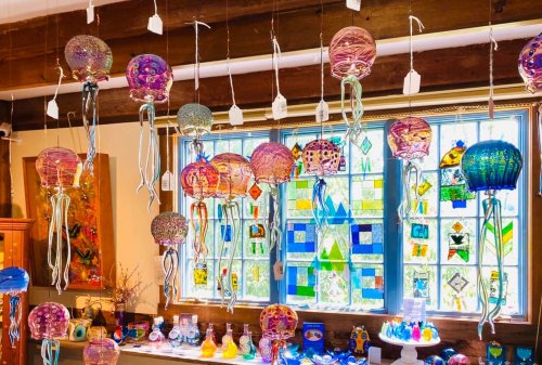 Colorful glass jellyfish hang from the ceiling, with a bright stained glass window in the background.