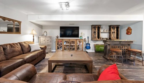 Cozy living room with leather sofas, a coffee table, a bar area, and a large TV on the wall. Warm, inviting atmosphere.