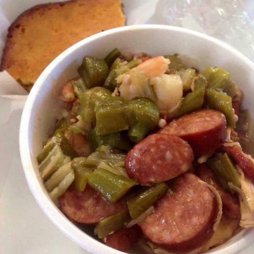 A bowl of gumbo with sausage, shrimp, and okra, served with a piece of cornbread on the side.