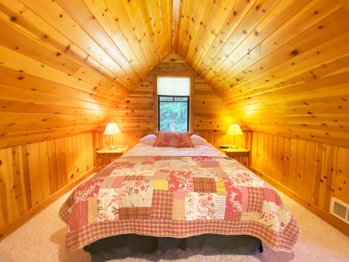 Cozy attic bedroom with wooden walls, a quilted bedspread, and two lamps on bedside tables.