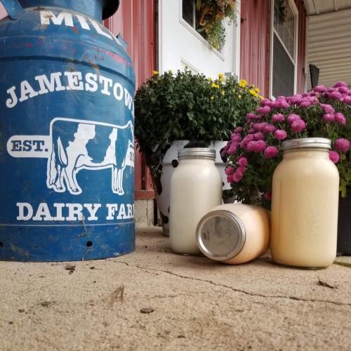 A vintage milk can beside jars of milk and flowers at Jamestown Dairy Farm, showcasing a rustic farm setting.