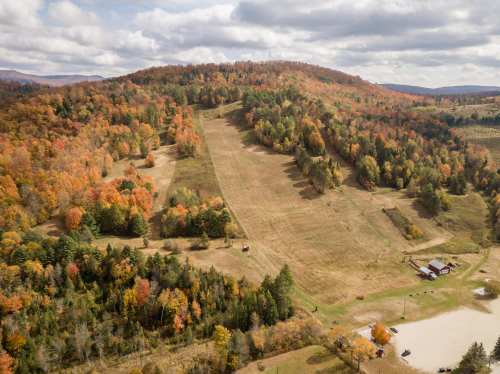 Aerial view of a hillside with autumn foliage, ski slopes, and a small building in a scenic landscape.