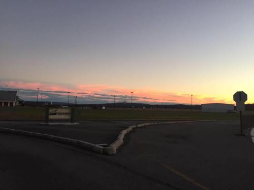 A serene sunset with pink and orange hues over a grassy field, with buildings and a stop sign in the foreground.