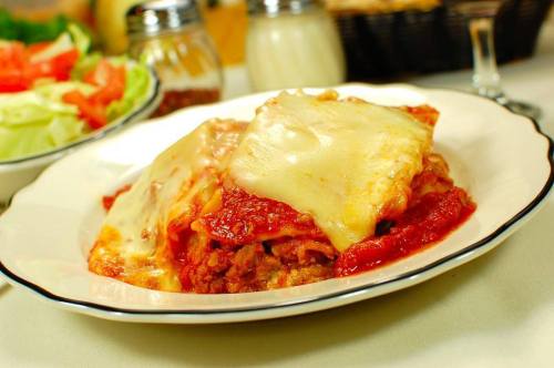 A plate of lasagna topped with melted cheese and marinara sauce, served with a side salad.
